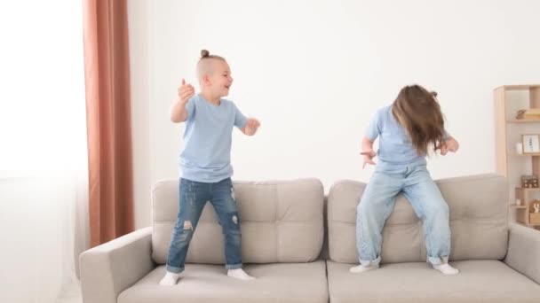 Energetische kleine kinderen broers en zussen springen blootsvoets op de bank, genieten van het vrije weekend vrije tijd samen thuis. - Video