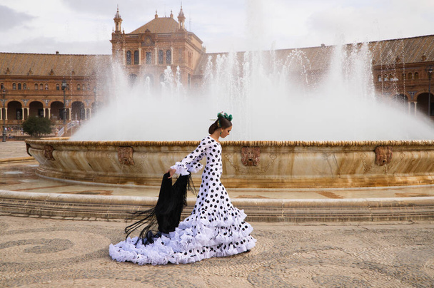 Γυναίκα χορεύτρια φλαμένκο, έφηβη μελαχρινή και όμορφη τυπική Ισπανίδα χορεύτρια χορεύει με ένα μαύρο σάλι μπροστά από ένα σιντριβάνι σε μια πλατεία στο Σεβάιλ. Φλαμένκο έννοια της παγκόσμιας πολιτιστικής κληρονομιάς. - Φωτογραφία, εικόνα