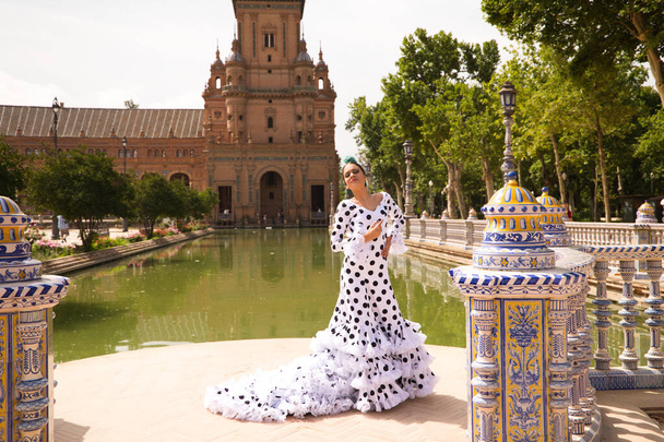 Bailarina flamenca, hermosa adolescente morena vestida con traje típico con volantes y lunares está bailando junto a un canal en una plaza del parque. Concepto flamenco del patrimonio cultural mundial. - Foto, imagen