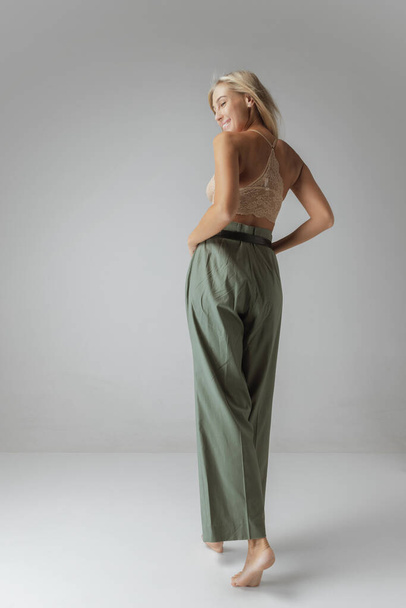 Tenderness. Attractive young woman with long blonde hair and natural makeup wearing crop top and casual trousers posing over grey background. Natural beauty, casualoutfit, inspiration, fashion and ad - Φωτογραφία, εικόνα