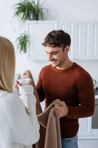cheerful man holding blanket near girlfriend in sweater with cup of tea - Photo, Image