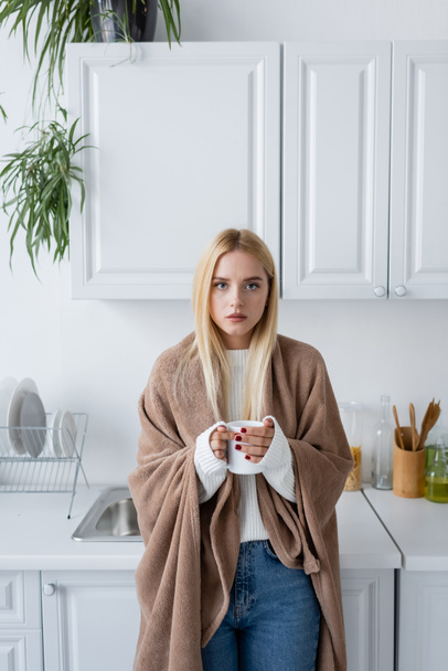 jovem mulher loira em suéter branco e cobertor segurando xícara de chá  - Foto, Imagem