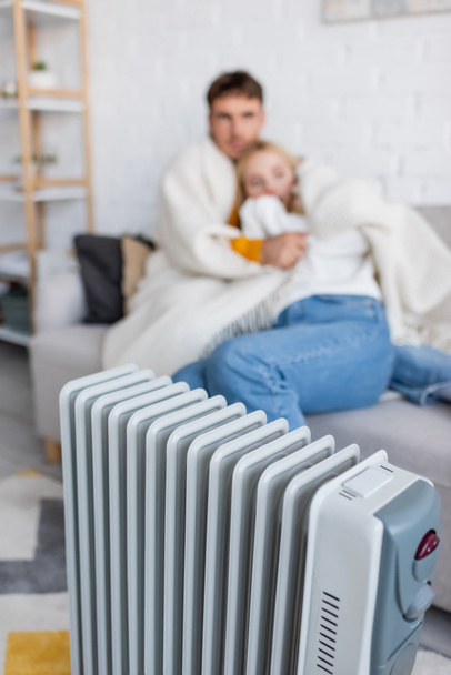 modern radiator heater near blurred couple hugging and sitting on couch under blanket  - 写真・画像