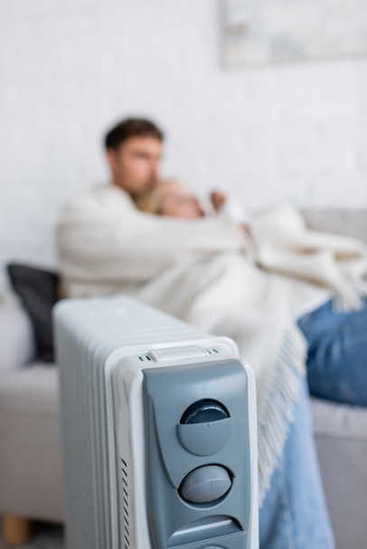 calentador de radiador moderno cerca de la pareja borrosa debajo de la manta en la sala de estar  - Foto, Imagen