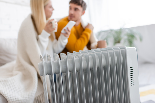 modern radiator heater near blurred couple covered with blanket  - Foto, afbeelding