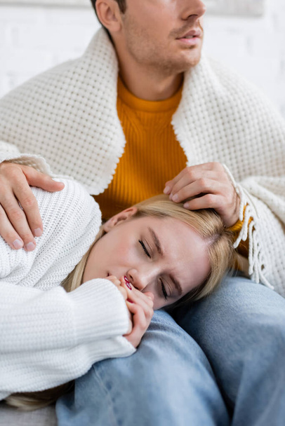 jeune femme couverte de couverture dormant sur les jambes du petit ami en jeans assis sur le canapé - Photo, image