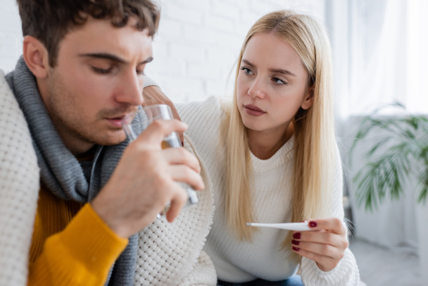 sick man drinking water near worried woman holding digital thermometer - Photo, Image