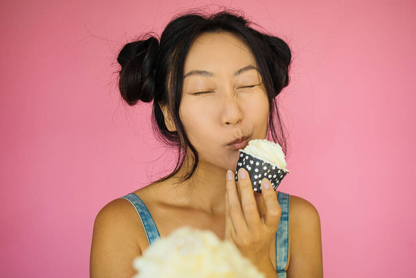 Afbeelding van mooie pin up aziatische vrouw geïsoleerd over roze muur achtergrond met een taart. - Foto, afbeelding