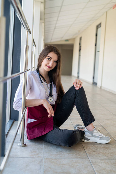A nurse with an attractive appearance in a uniform is waiting for patients in the clinic in the corridor. The concept of a female portrait. A doctor in a uniform - Foto, Imagen