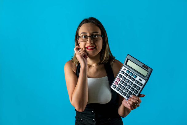 青い背景に隔離された眼鏡を身に着けて叫んで計算機を保持している若いブルネットの女性のCEOの写真。仕事だ。ビジネスレディー。厳格な女性の肖像画です - 写真・画像