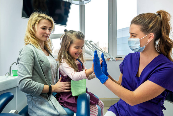 Мати маленької дівчинки і стоматолог заспокоюють маленьку дівчинку перед лікуванням зубів. Концепція підходу до дітей в стоматології
 - Фото, зображення