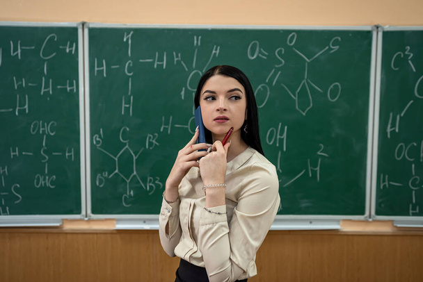 молодий красивий вчитель вчить урок хімії і стоїть біля дошки з хімічною формулою, концепція освіти
 - Фото, зображення