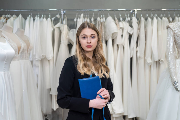 female seller hold pen and notes near wedding dress in boutique. Wedding day - 写真・画像