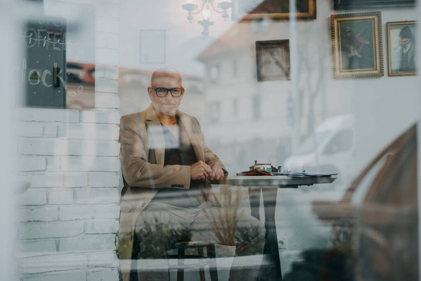 Elegant senior man sitting in a cafe and looking out of window. - Foto, imagen