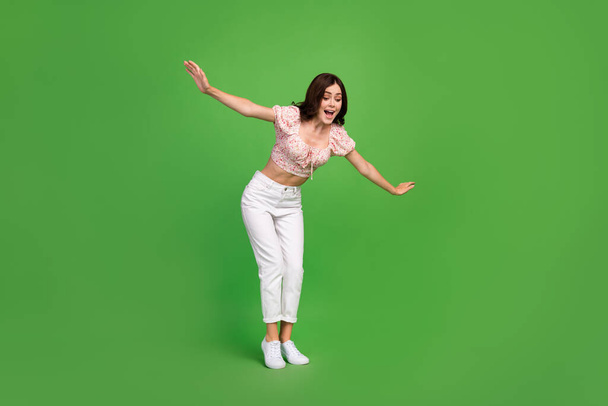 Full length photo of pretty woman with curly hairdo wear white trousers blouse look down hold balance isolated on green color background. - Фото, изображение