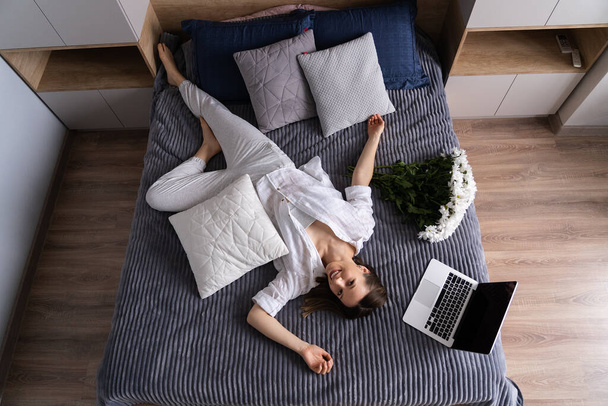 Кавказка в белой повседневной одежде, расслабляющая во время использования ноутбука на кровати - Фото, изображение