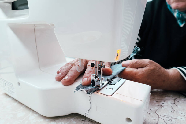 Vista della macchina da cucire con mano. Un vecchio sarto maschio cuce su una macchina da cucire elettrica. Primo piano sulle mani. - Foto, immagini