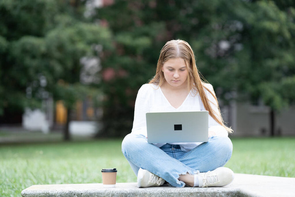 Adolescente universitaria estudiante sentada en el banco y el uso de la computadora portátil al aire libre en el parque. Freelancer o nómada digital concentrado en ordenador. - Foto, imagen