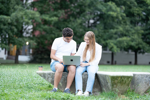 Δύο έφηβοι μαθητές που εργάζονται σε φορητό υπολογιστή έξω σε ένα πάρκο. - Φωτογραφία, εικόνα