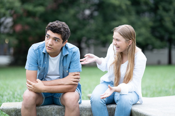 Znudzony nastolatek chłopiec słuchając podekscytowany dziewczyna mówi zbyt wiele na zewnątrz w parku - Zdjęcie, obraz