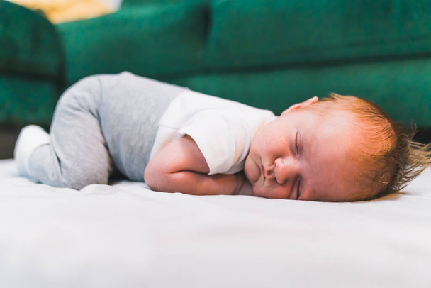 Its time for a baby nap. Cute caucasian infant baby boy in gray sweatpants and white t-shirt sleeping on his belly on soft portable mattress for children. High quality photo - Foto, Bild