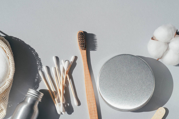 Zero waste concept. Metallic bottle and can, reusable cotton rounds. Packaging for cleaning teeth without plastic. Wooden toothbrush and glass jar with toothpaste on a grey background. Bathroom accessories, oral care - Photo, Image