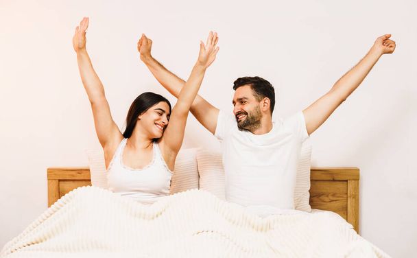 Happy couple waking up with raised hands, feeling good in the morning at home. High quality photo - 写真・画像