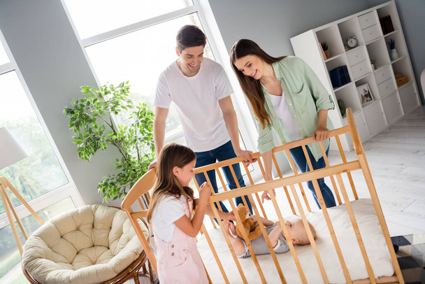 Photo of peaceful friendly family spend pastime together near toddler crib house indoors. - Zdjęcie, obraz