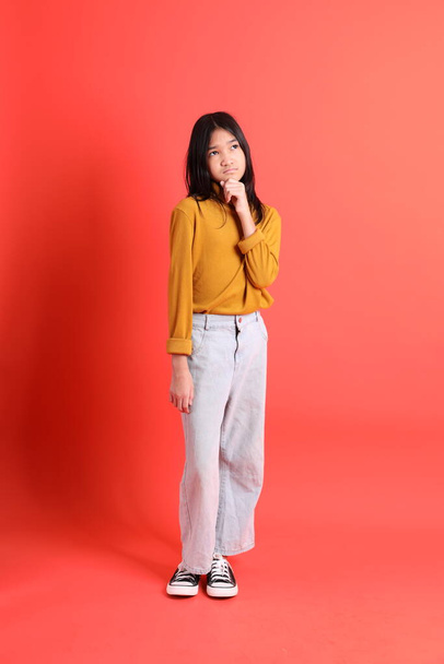 The young Asian girl with yellow shirt on the orange background. - Valokuva, kuva