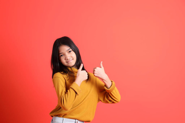 The young Asian girl with yellow shirt on the orange background. - Photo, image