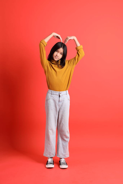 Mladá asijská dívka se žlutou košilí na oranžovém pozadí. - Fotografie, Obrázek