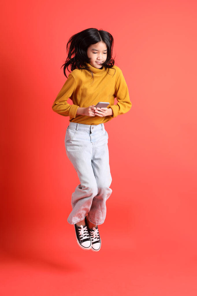 Das junge asiatische Mädchen mit dem gelben Hemd auf dem orangefarbenen Hintergrund. - Foto, Bild