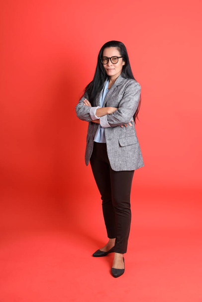 The Asian senior businesswoman standing on the orange background. - Foto, afbeelding