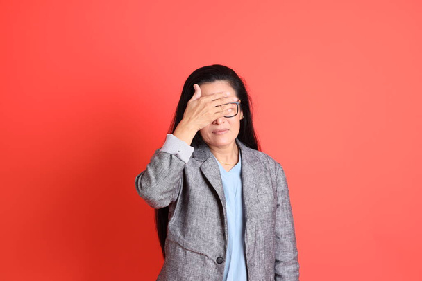 The Asian senior businesswoman standing on the orange background. - Φωτογραφία, εικόνα