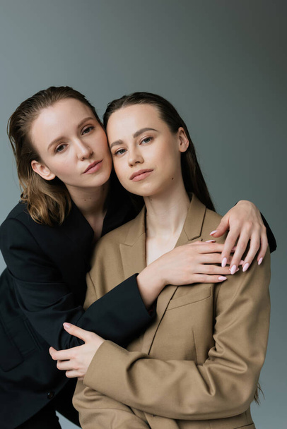 young and pretty lesbian women in black and beige blazers looking at camera isolated on grey - Fotoğraf, Görsel