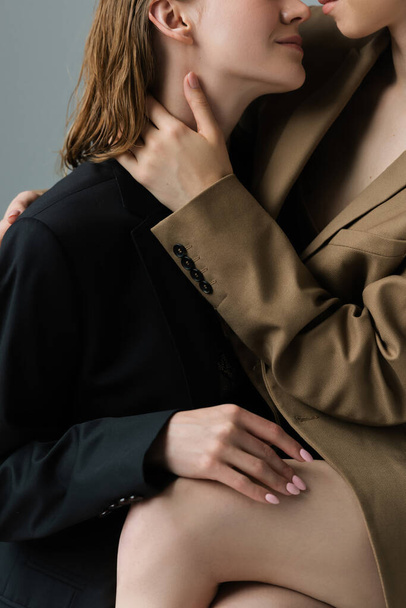 partial view of same sex lesbian couple in beige and black blazers embracing isolated on grey - Fotoğraf, Görsel