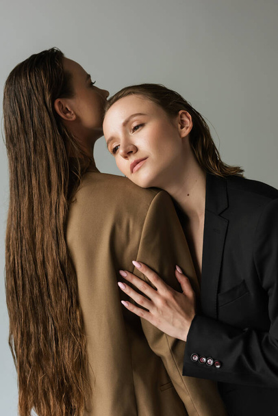 sensual lesbian woman leaning on long haired girlfriend isolated on grey - 写真・画像