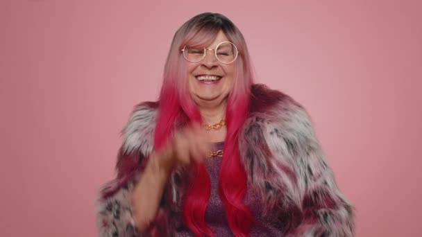 Χαρούμενη κομψή ηλικιωμένη γυναίκα να γελάει δυνατά αφού άκουσε ένα γελοίο ανέκδοτο, αστείο αστείο, αισθανόμενη ανέμελη διασκέδαση, θετικός τρόπος ζωής των ανθρώπων. Ανώτερη γιαγιά απομονωμένη σε ροζ φόντο στούντιο - Πλάνα, βίντεο