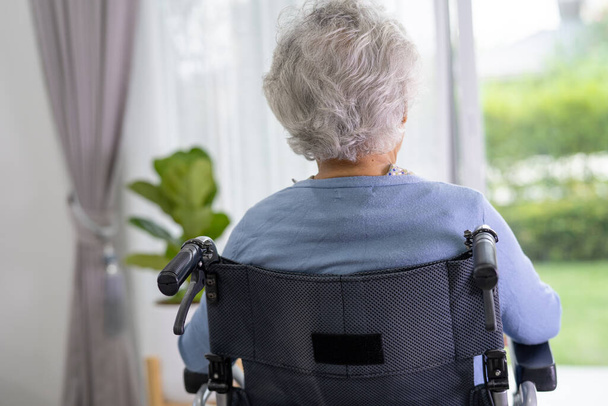 Een oudere vrouw die op een rolstoel zit en uit het raam kijkt omdat ze op iemand wacht. Helaas, melancholie en depressief. - Foto, afbeelding