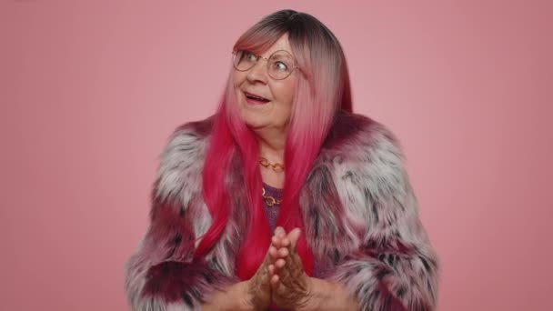 Sneaky cunning woman with tricky face gesticulating and scheming evil plan, thinking over devious villain idea, cunning cheats, jokes and pranks. Senior grandmother on pink studio background indoors - Footage, Video