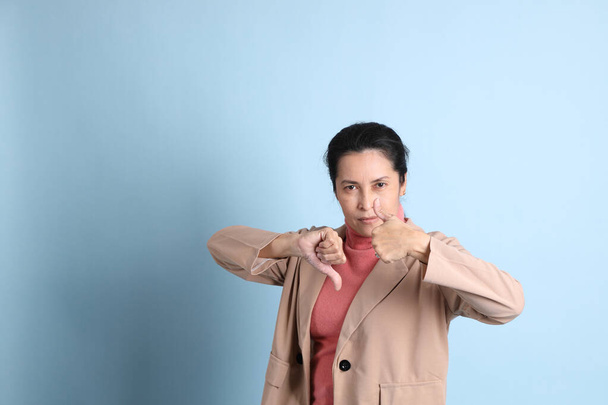 La mujer asiática senior con camisa rosa chaqueta marrón sobre el fondo azul. - Foto, imagen