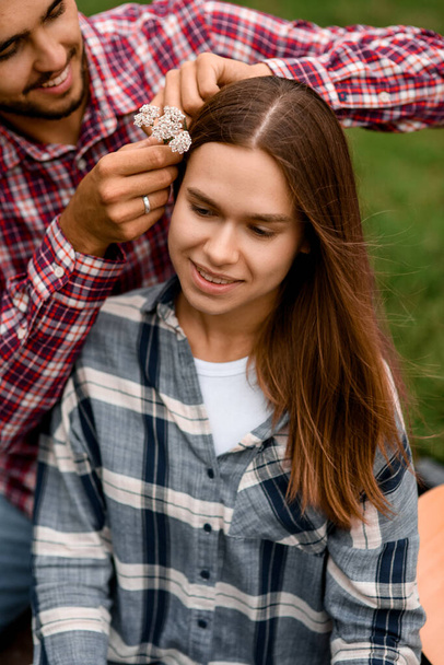 close-up of young smiling woman whose man decorates her hair with flowers. Romantic atmosphere. Love story. - Foto, imagen