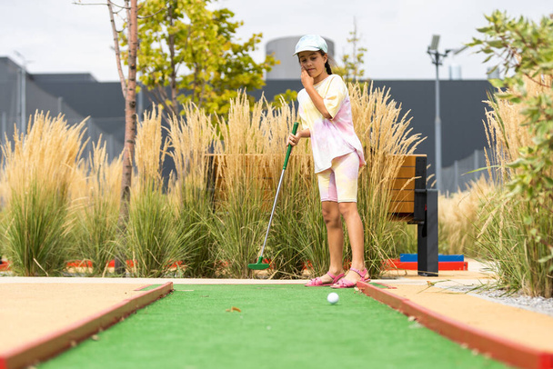 Cute preschool girl playing mini golf with family. Happy child having fun with outdoor activity. Summer sport for children and adults, outdoors. Family vacations or resort - Fotografie, Obrázek