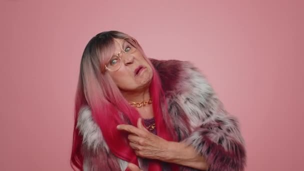 Смешная, радостная, искренняя пожилая женщина 70 лет в пальто, делающая игривые глупые мимические мимики и гримасы, валяющая дурака, показывая язык. Старшая бабушка изолированы в одиночку на розовом фоне стены - Кадры, видео