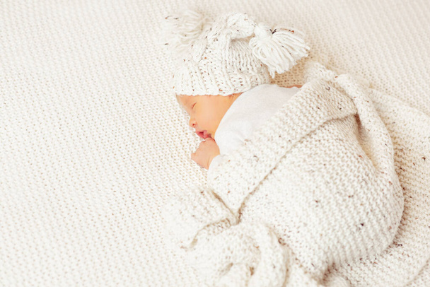 Newborn Sleeping on Stomach. Cute Baby in knitted Hat covered with Woolen Blanket. Infant Child sleep lying down on White Bed. New born Boy dreaming - Photo, Image