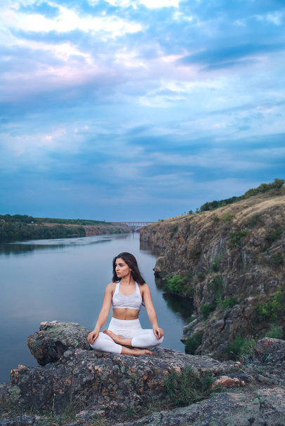 少女は岩の上の川岸にヨガの蓮の瞑想の場に座っています - 写真・画像