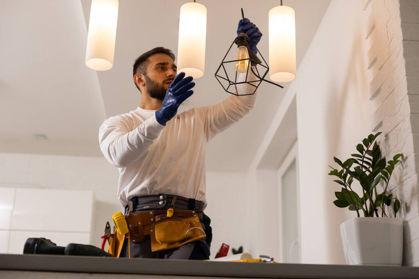 Electrician worker man assembling electric lamps in new apartment - Foto, Imagen