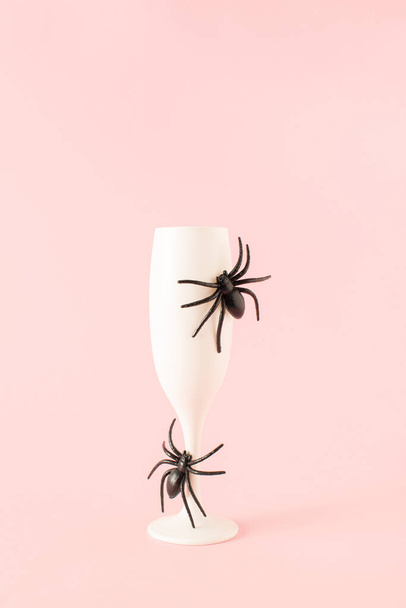 Kreative Idee aus Champagnerglas mit Spinnen auf pastellrosa Hintergrund. Minimales Halloween-Party-Konzept. - Foto, Bild