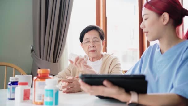 Asiatische Krankenschwester hält eine Medikamentenflasche in der Hand und teilt der asiatischen Seniorin Informationen mit, bevor sie Medikamente verabreicht. Besuch von Pflegekräften zu Hause. Gesundheitskonzept für zu Hause. 4k Zeitlupenvideo. - Filmmaterial, Video