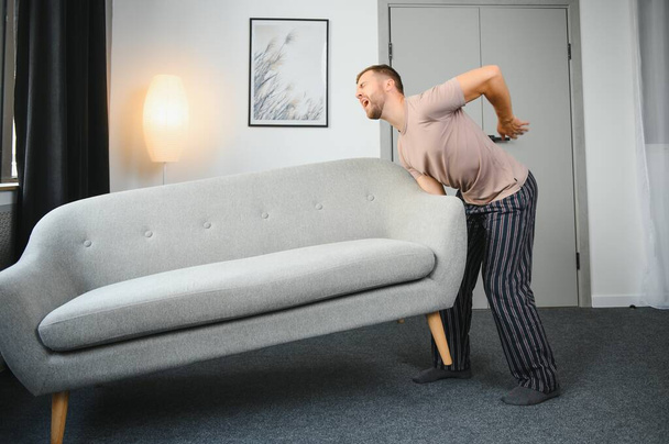 Young man suffering from back pain after carrying heavy furniture - Фото, изображение